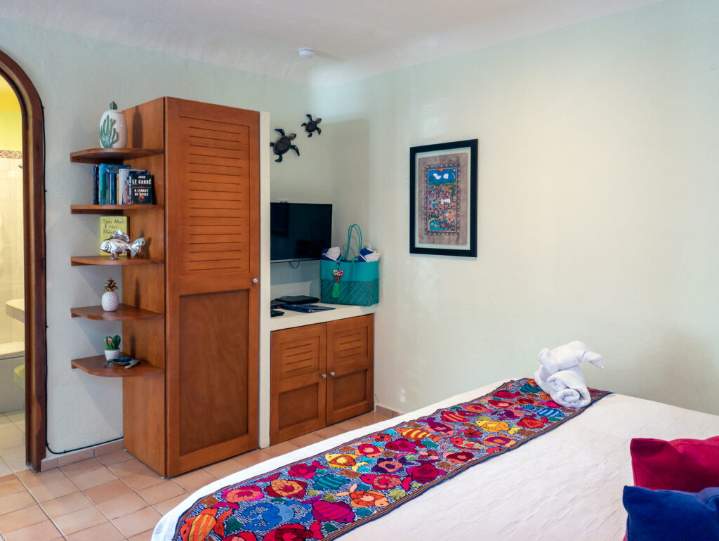 Bed with a floral runner facing a wooden storage cabinet, shelves, and television.