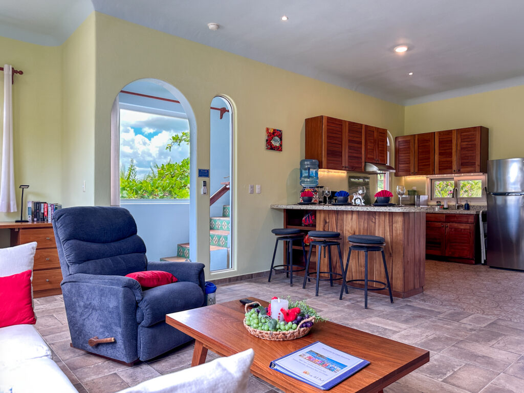 Blue recliner and coffee table beside an arched doorway and the open kitchen breakfast bar.