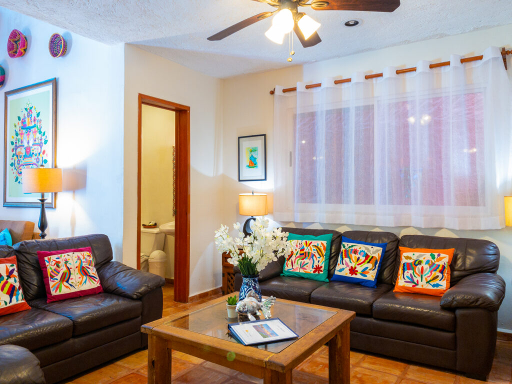 Dark sofas with colorful patterned cushions around a wooden coffee table beside a bathroom doorway.