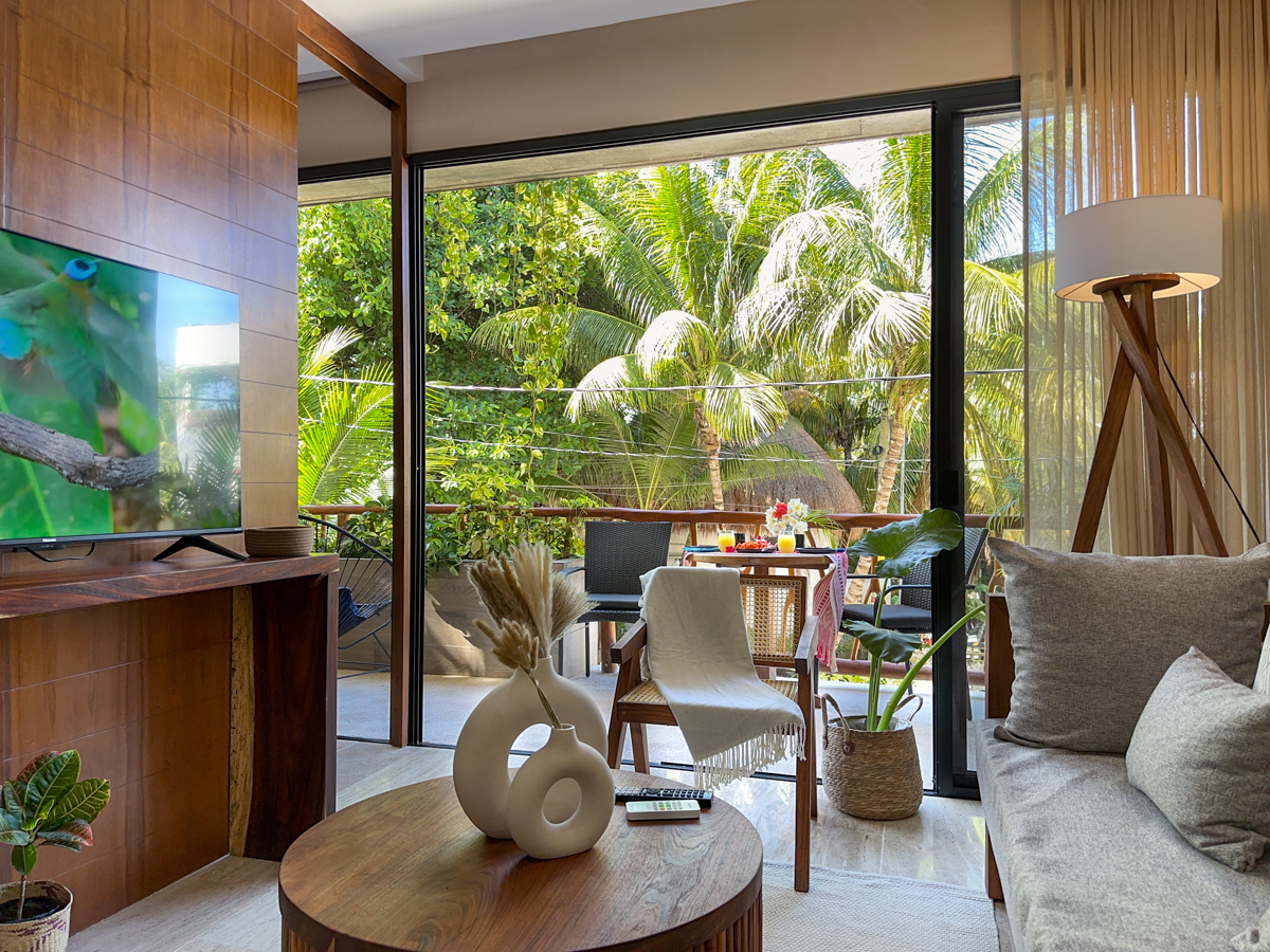 Television and round coffee table beside wide balcony doors overlooking dense palms.